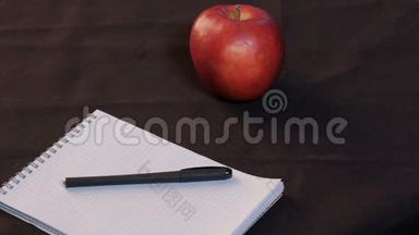 手少年特写.. 那个年轻人从桌子上举起眼镜。 <strong>一个红苹果</strong>，<strong>一个</strong>笼子里的记事本和一支钢笔躺在上面
